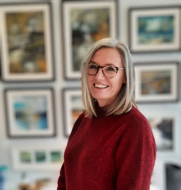 Kymme Fraser - contemporary Scottish Artists, standing in front of a wall of framed paintings